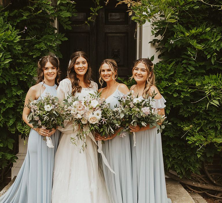 Bridal party shot with the bridesmaids in pretty pastel blue dresses and bride in a balloon sleeve dress with pink and white wedding flowers 