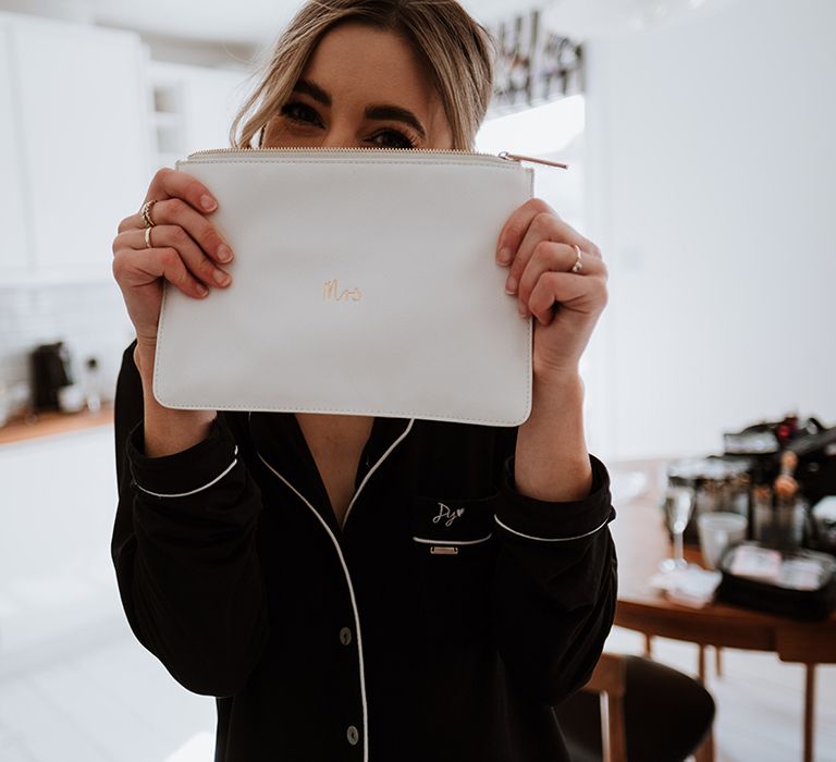 Bride wears black pyjamas and holds up white bridal purse 