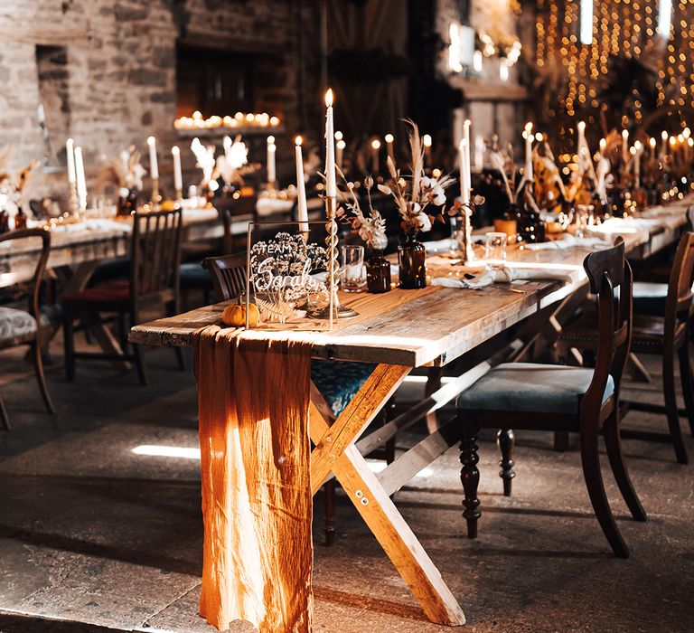 Wooden banquet tables for barn reception complete with burnt orange fabric table runner and candles 