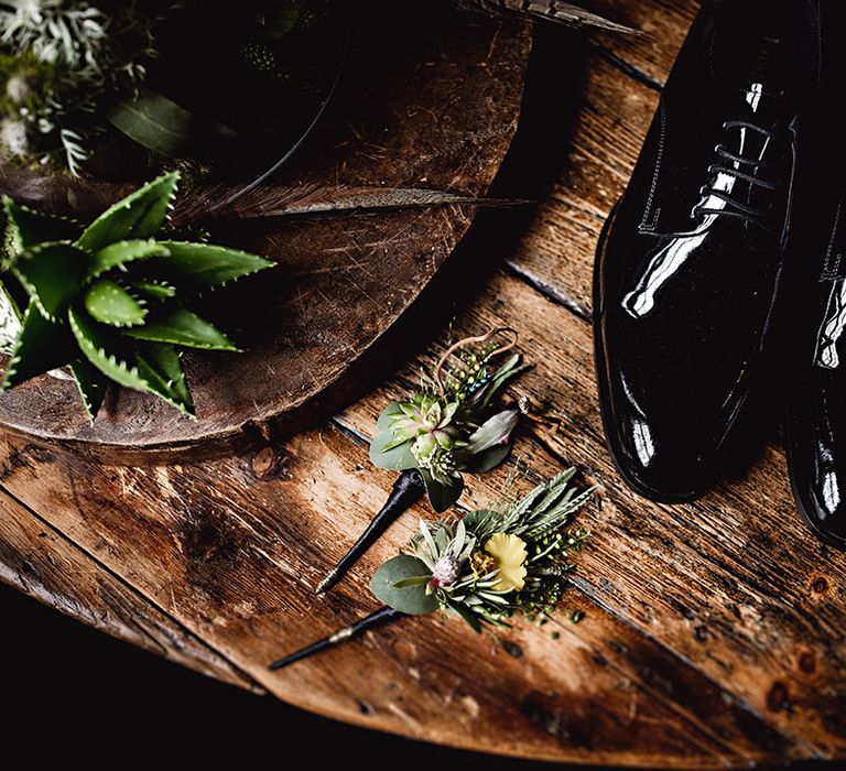 Patent black shoes beside floral buttonholes on wooden table