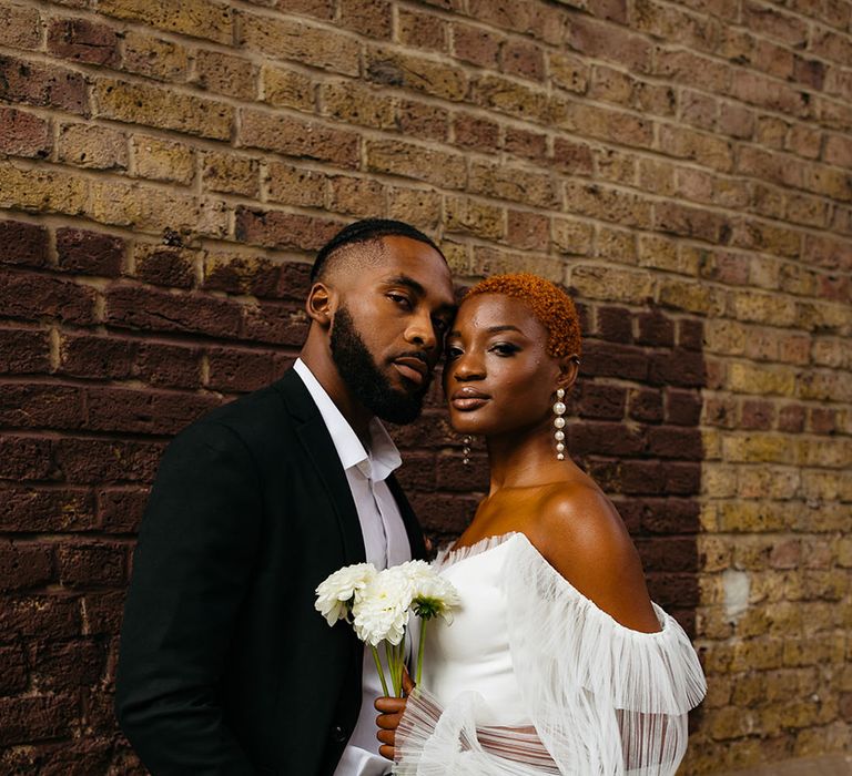 Bride wearing pearl drop earrings and off shoulder puff lace sleeves with leg slit and groom in smart black suit 