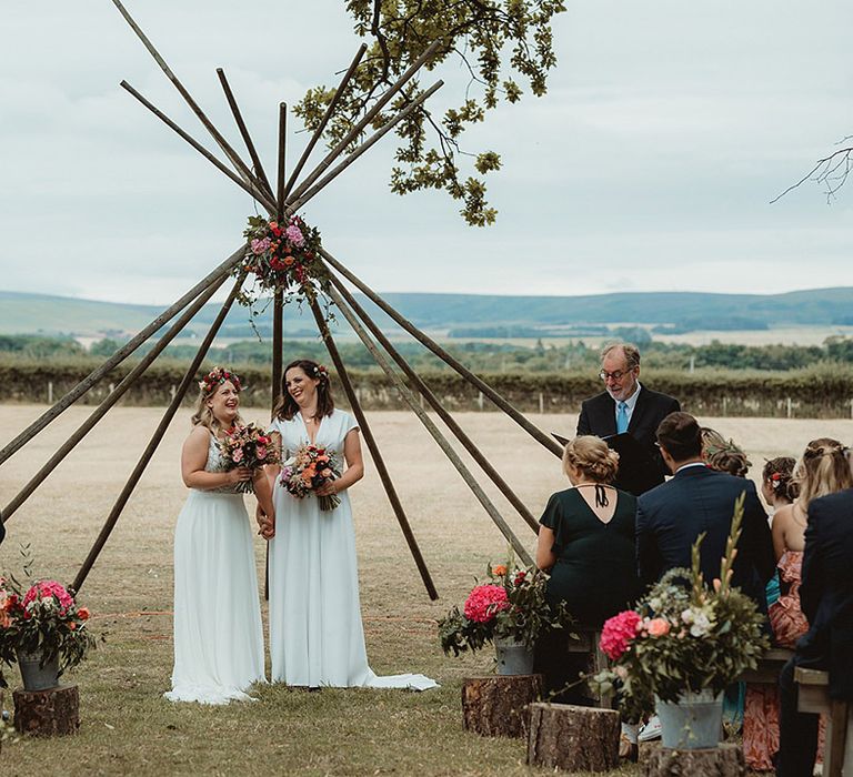 Tree stumps decorate the aisle with colourful pink and orange flowers with the brides standing at the altar for their lesbian wedding 