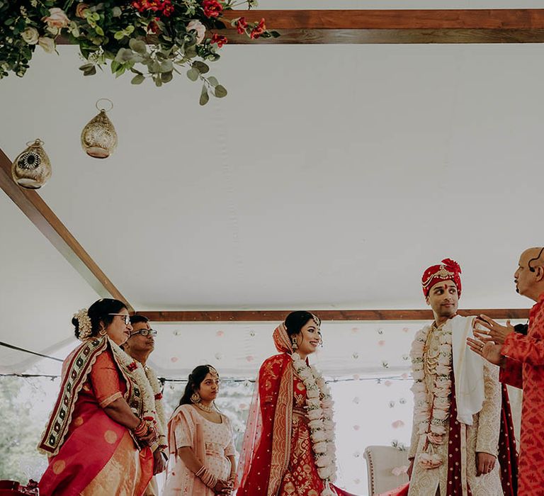 Bride in red and gold lehenga and groom in red, white and gold sherwani during wedding ceremony 