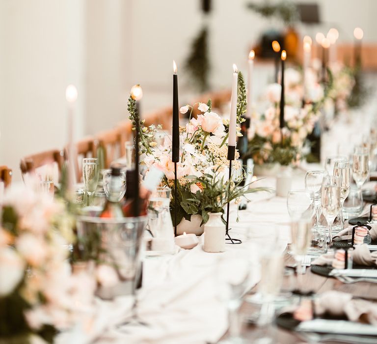 Close up of off-white table runner, black and light pink tapered candles, foliage and rose arrangements and hanging foliage decor