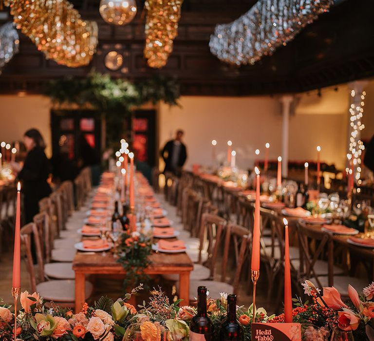 Head table of Christmas multicultural London wedding with streamer decorations, orange flower and foliage table runners, orange tapered candles and suspended foliage decor