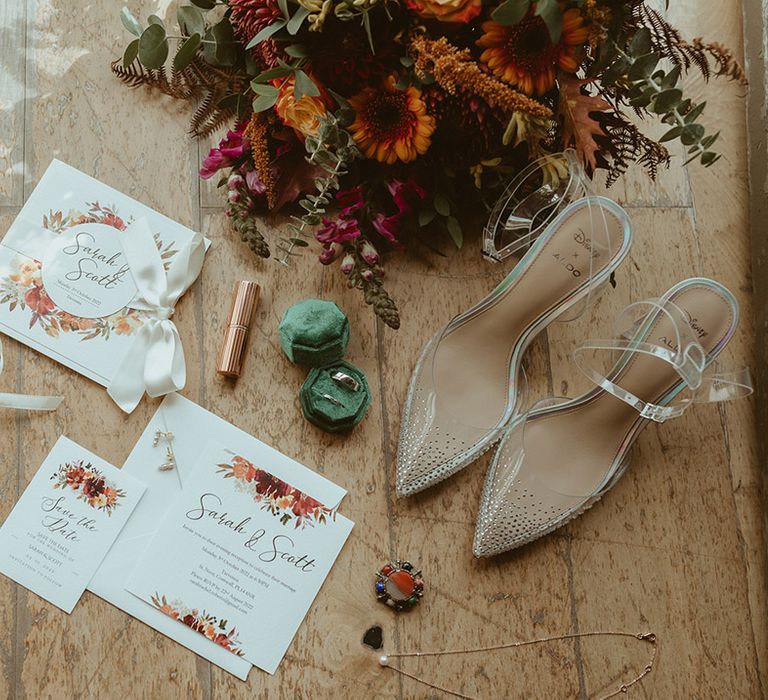 Autumn leaf theme wedding stationery with the bridal bouquet, Charlotte Tilbury lipstick, green velvet ring box and wedding bands with sparkly Cinderella wedding shoes