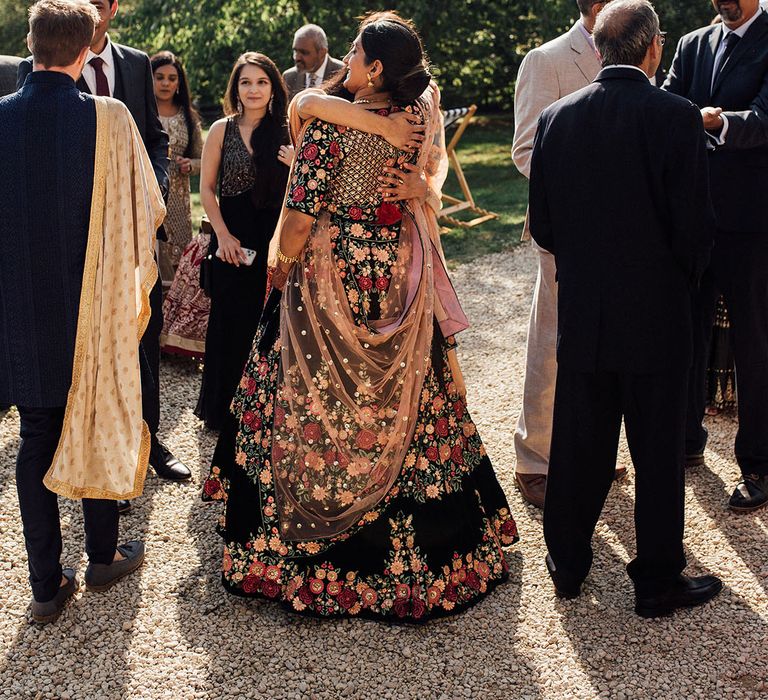 Indian bride in colourful and embellished lehenga hugs wedding guest at the Longbourn Barn Estate 