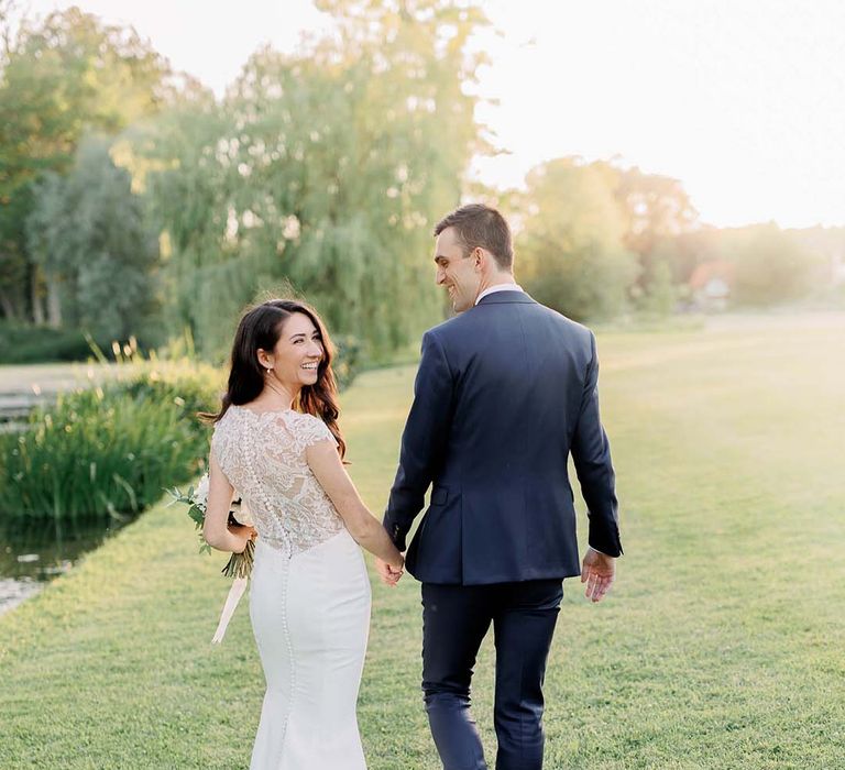 bride in a lace back Kelly Faetanini fitted wedding dress holding hands with her groom in a navy suit