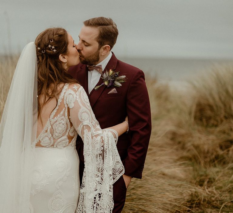 Bride in boho bell sleeve wedding dress and gold star hair accessories with the groom in burgundy suit 