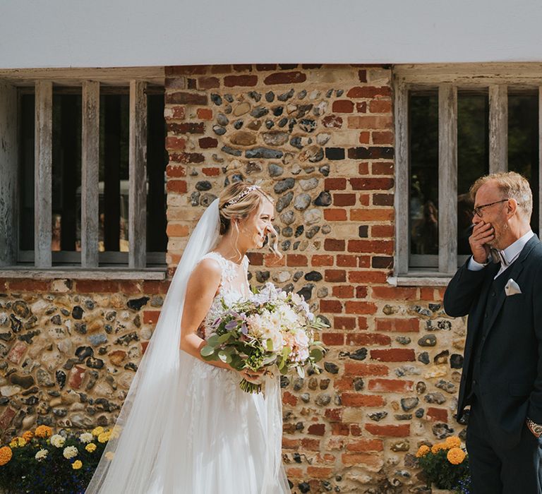 Father of the bride in a navy suit and silver bow tie gets emotional as he sees the bride in her wedding dress for the first time 