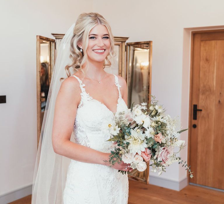 Bride in fitted lace wedding dress and veil with her blonde hair in a half up half down hairstyle with all white wedding bouquet 