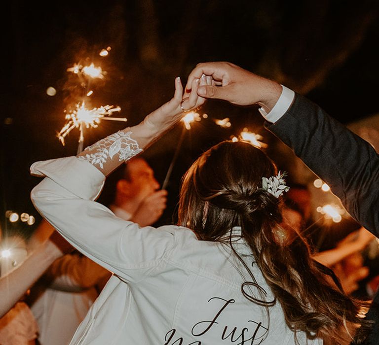 The groom twirls the bride who wears a white denim jacket with black font reading 'Just Married'