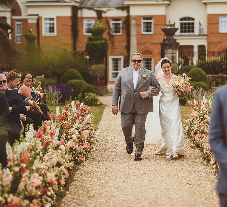 Father of the bride in light grey suit with black sunglasses walking with bride down the aisle 