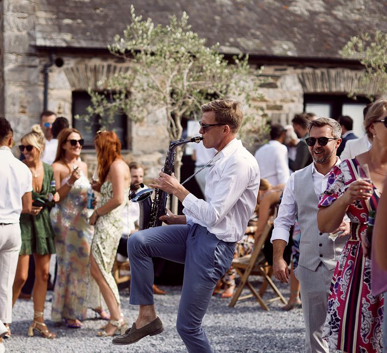 Saxophonist plays at wedding during cocktail hour  