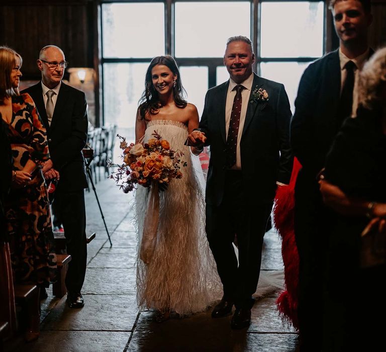 Bride in strapless ivory fringed crepe gown and chapel length veil walking down the aisle at Willow Marsh Farm Loughborough 