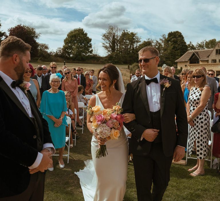 Bride holding colourful pink and orange rose and gypsophila bouquet walking down the aisle with her father 