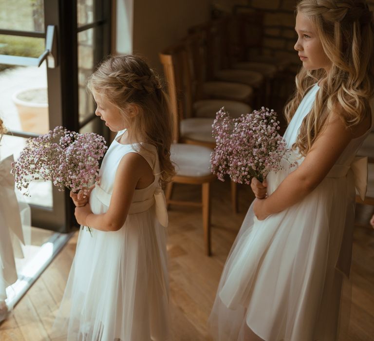 Flower girls in pretty white dresses tied with bows holding bouquets of gypsophila 