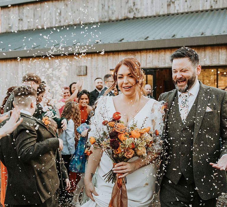 The bride and groom walk out of their wedding to white confetti being thrown by their guests 