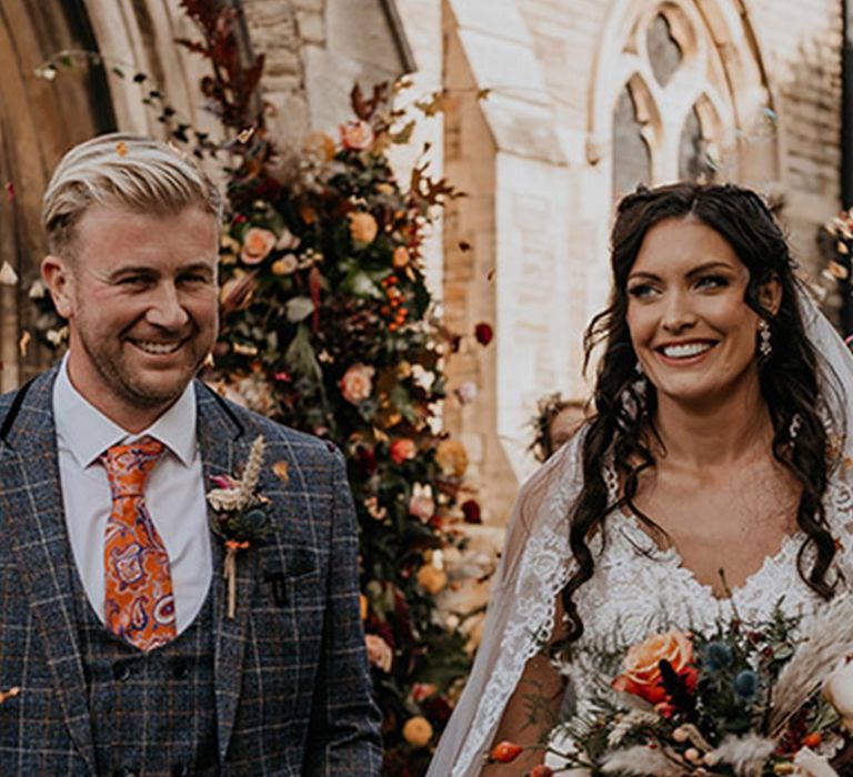 Bride holding an autumnal cascading bouquet walking with the groom wearing an orange paisley tie 