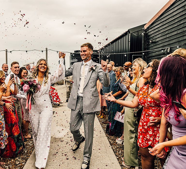 confetti moment at East Quay Whitstable wedding venue with the bride in a wide eg and long sleeve jumpsuit and groom in a light grey suit and loafers