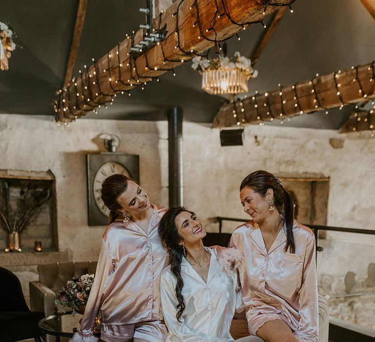 Bridesmaids in pink satin pyjamas with the bride in white pyjamas on the morning of the wedding 