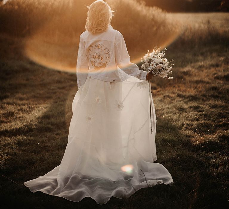 Golden hour wedding photo of bride in daisy Freda Bennett Brady wedding dress with bespoke white denim jacket 