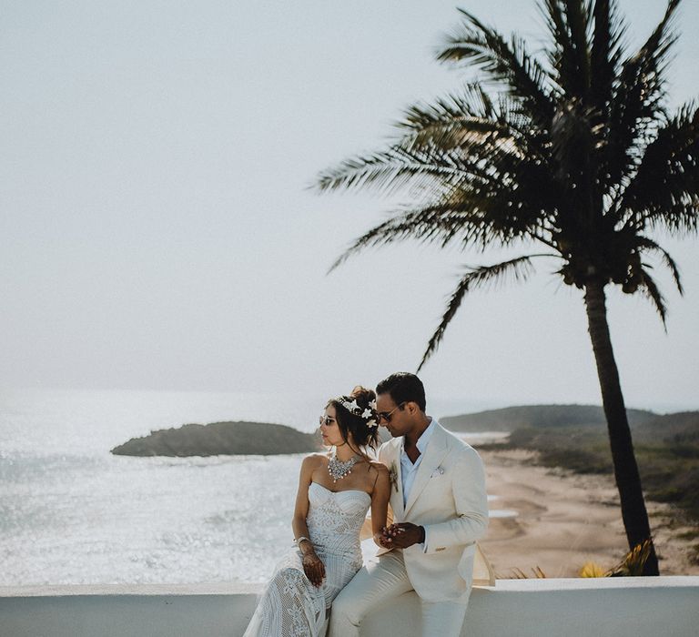 Bride and groom sitting in front of ocean at boho Tigre Del Mar wedding wearing sunglasses 