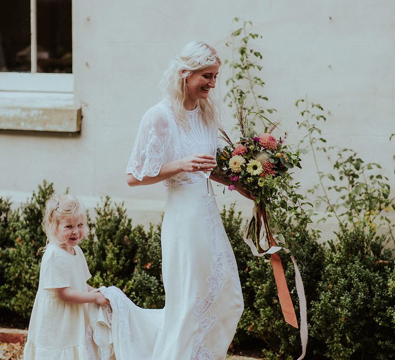 Bride walking in gorgeous ASOS wedding dress being held by a flower girl in a white dress 