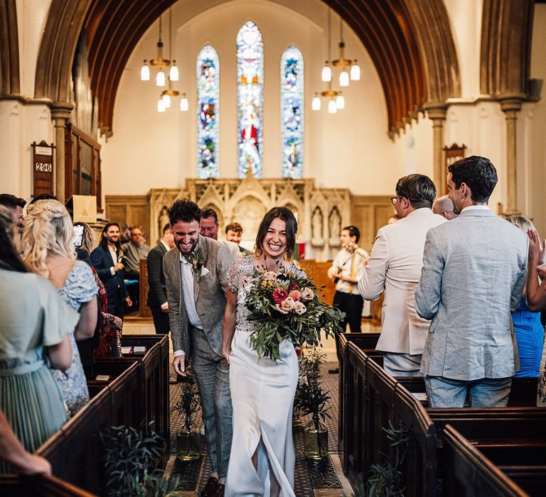 Smiling bride and groom walking back down the aisle together as a married couple 