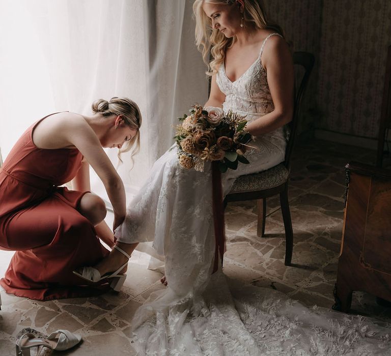 Bride in boho lace wedding dress with bridesmaid in terracotta bridesmaid dress helping the bride put on her shoes 