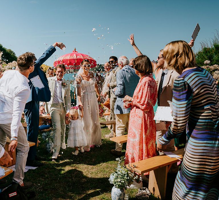 Guests throw confetti in celebration as the bride and groom walk back down the aisle as a married couple 