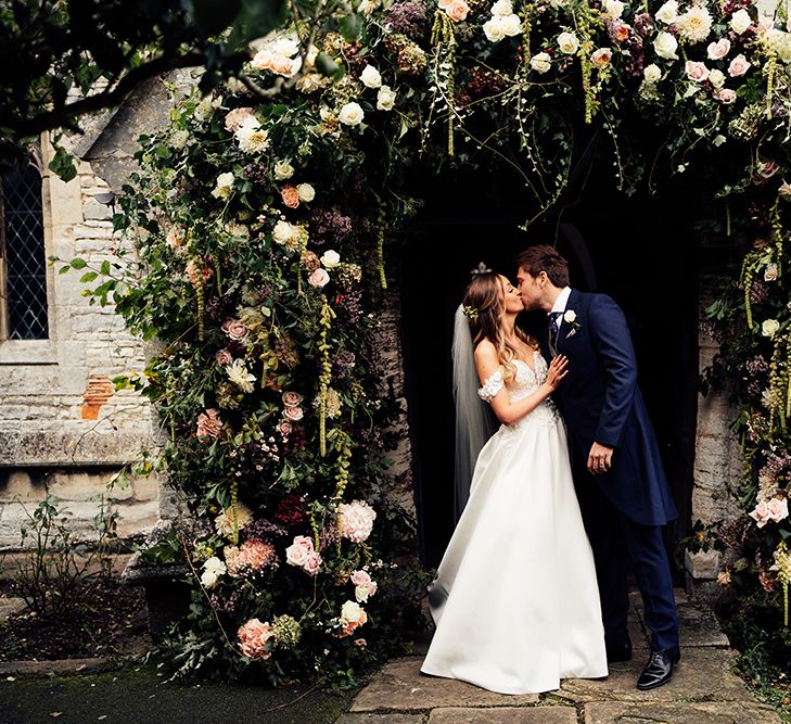 Newly wed couple kissing at barn wedding with flower arch