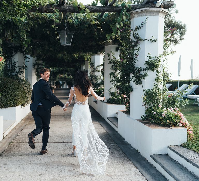 Bride and groom skipping through Villa Cimbrone in Ravello, Italy wearing an appliqué bridal jumpsuit