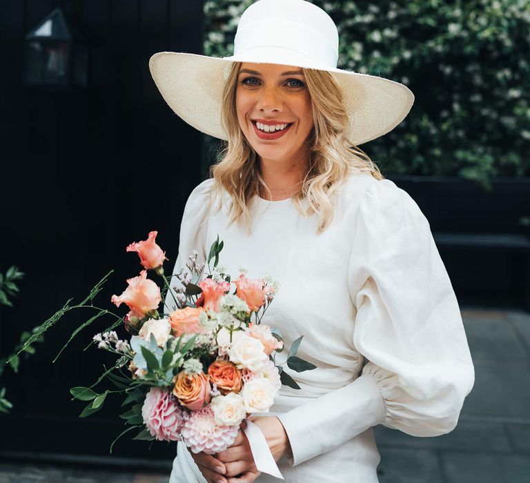 Happy London bride wearing white bridal hat and pink and peach bridal bouquet 