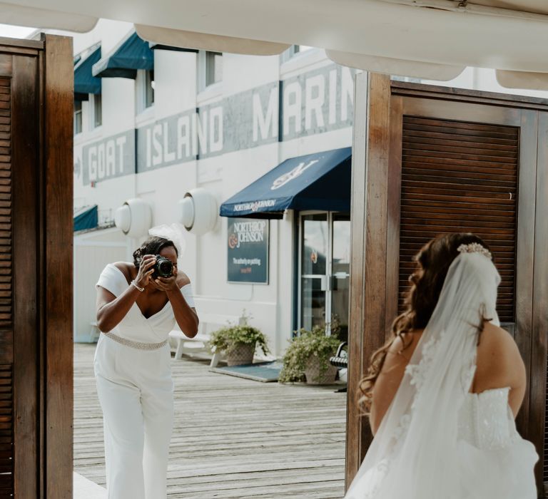 Black bride in an off the shoulder jumpsuit and flat shoes taking pictures of her bride 