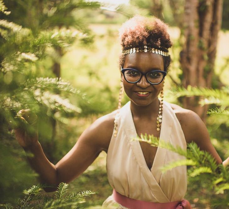 A bride in a ink gown wears her afro hair curly on top and short to the sides. She wears a metallic head piece.