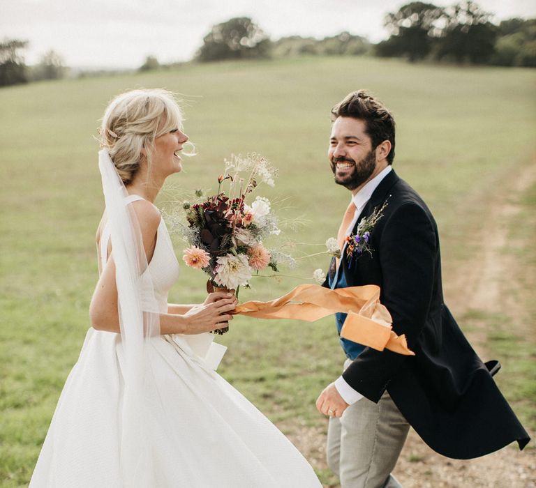 Classic bride and groom dancing in a field holding a wildflower wedding bouquet tied with ribbon 