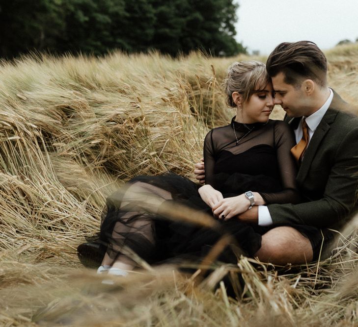 Bride & groom sit together in golden fields on wedding day