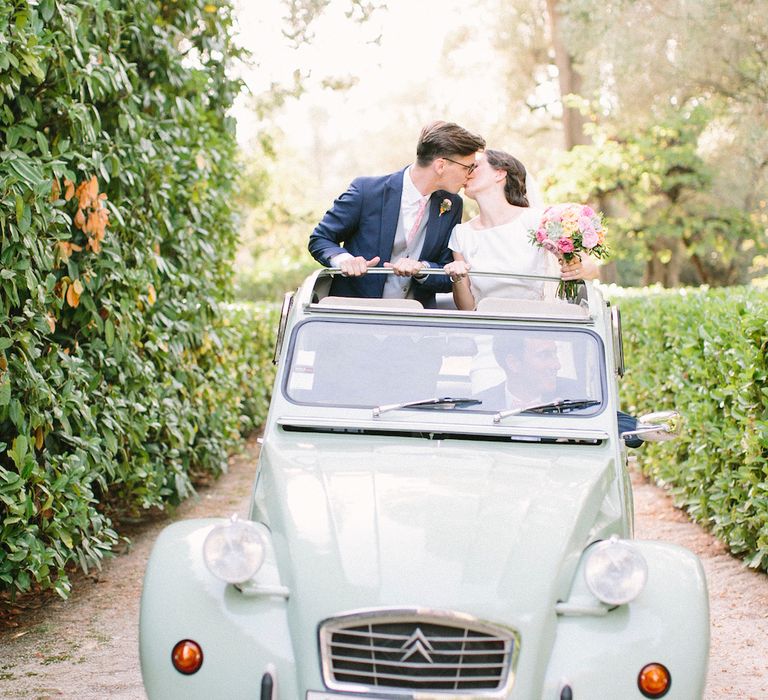 A pale green citroen at French wedding with its roof down.  A bride and groom kissing out of the roof. Photography by Saya Photography.