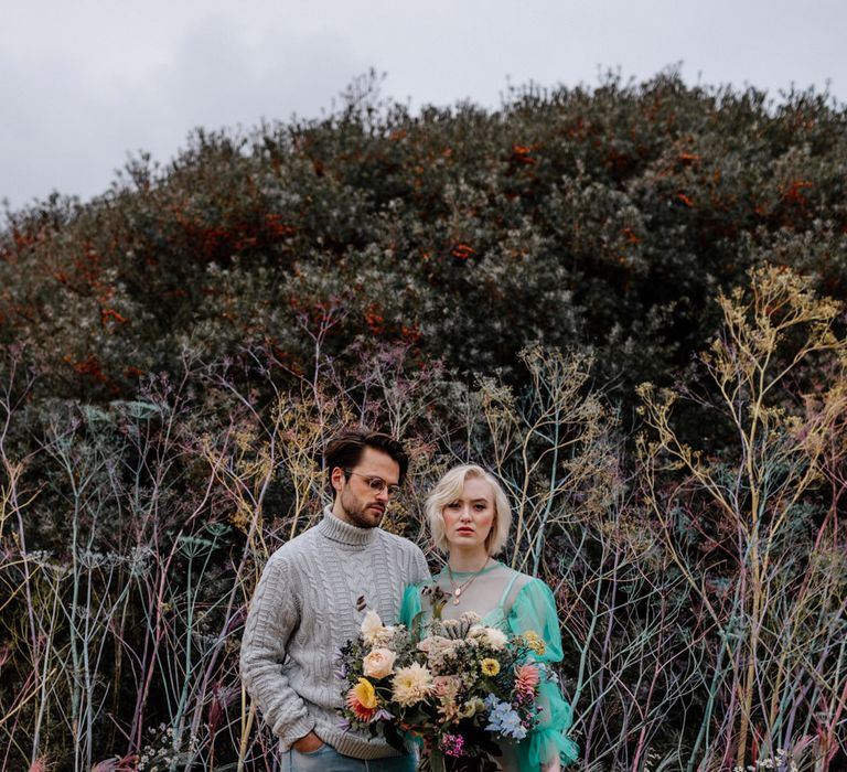 Contemporary couple at a colourful beach elopement with the bride in a sheer green wedding dress and the groom in a wooly jumper