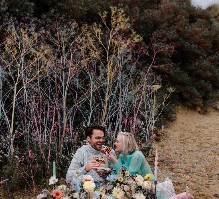 Intimate pizza picnic on the beach with pastel flowers and candles staked in the sand 