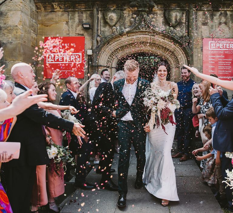 Bride & groom leave church with confetti being thrown around them on their wedding day