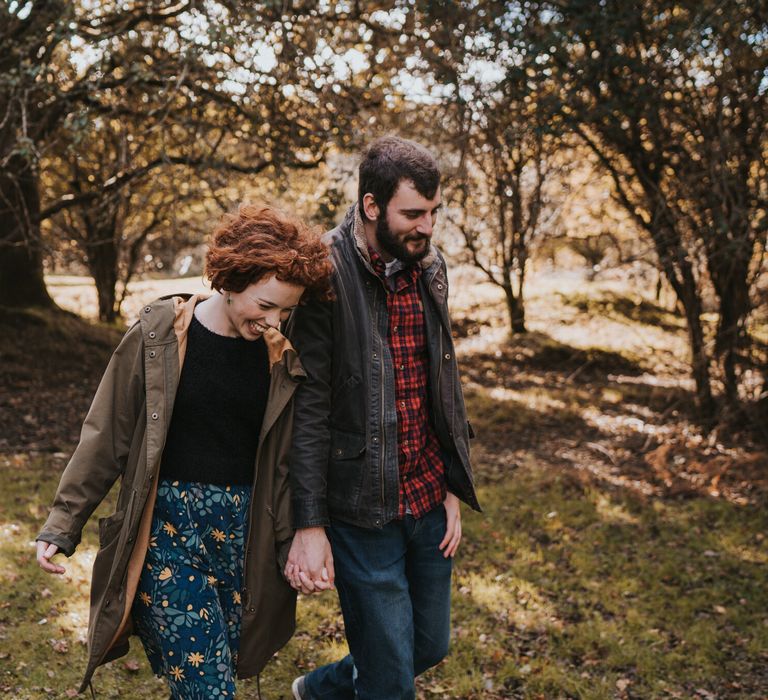 Engaged couple walk through the forest whilst the sun shines through