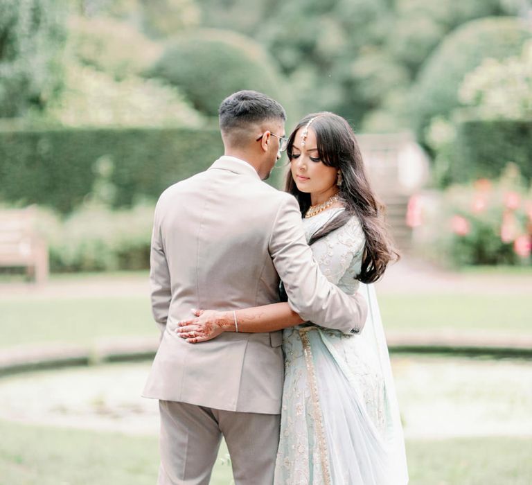 Muslim bride in a mint green sari and henna art with her hands around her husband in a sand coloured suit