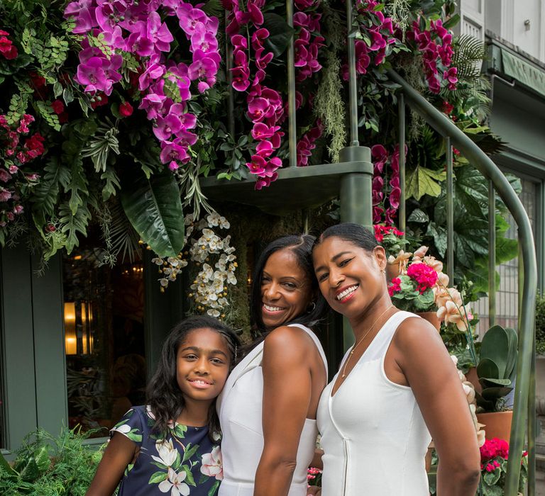 Bridal party portrait with flower girl in a navy floral dress and bridesmaid in a white knee length dress