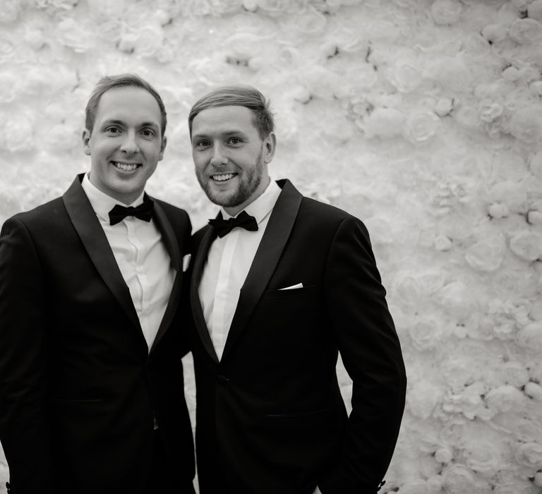 Grooms smile in front of flower wall in black & white image