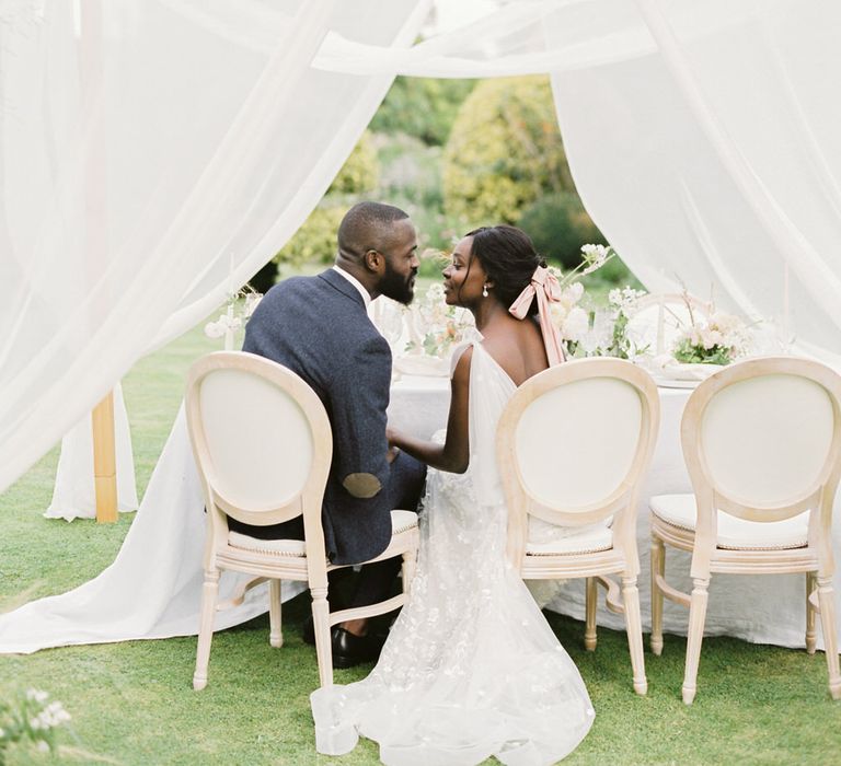 Bride and groom sitting underneath a pergola at their English garden party wedding reception