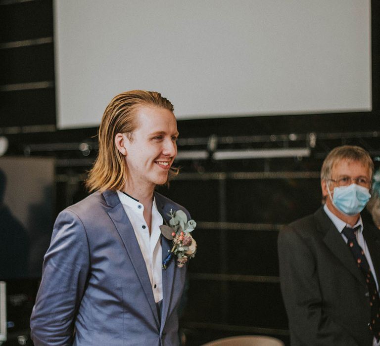 Groom in a light blue suit with white grandad shirt waiting at the altar for his bride