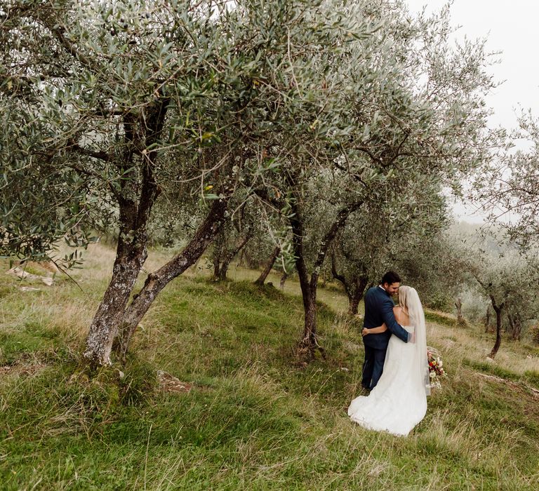 The bride and groom walk arm in arm through an olive grove at Podere Conti