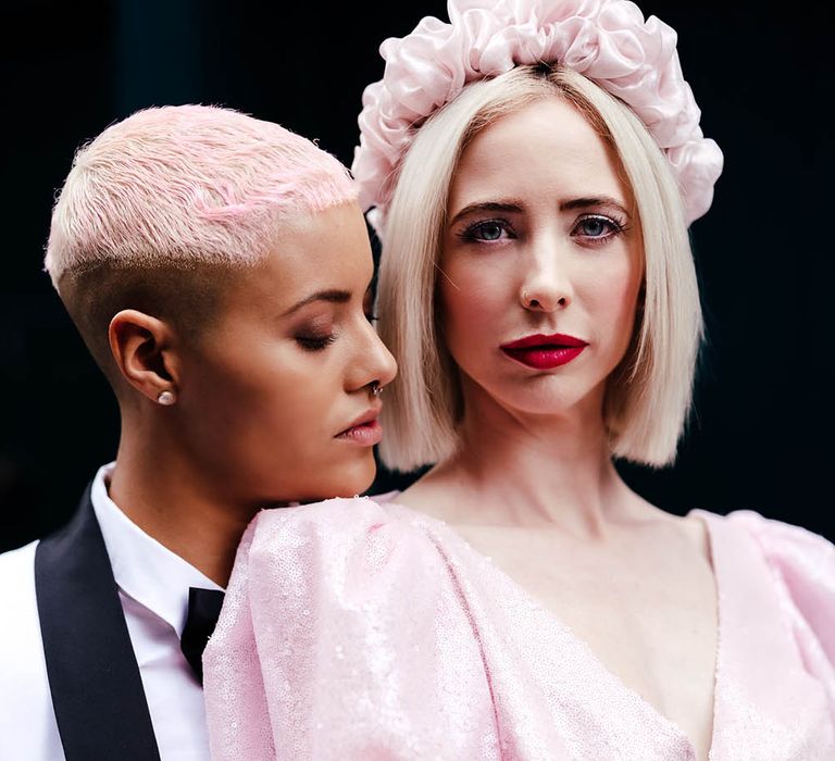 Bride with short pink hair embracing her bride in a pink jumpsuit with blonde bobbed hair and red lipstick 